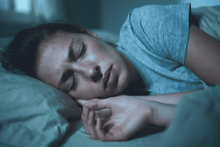 Junge Frau liegt nachts wach im Bett mit Hand am Kiefer – Ursachen von Zähneknirschen, JUST KFO Köln